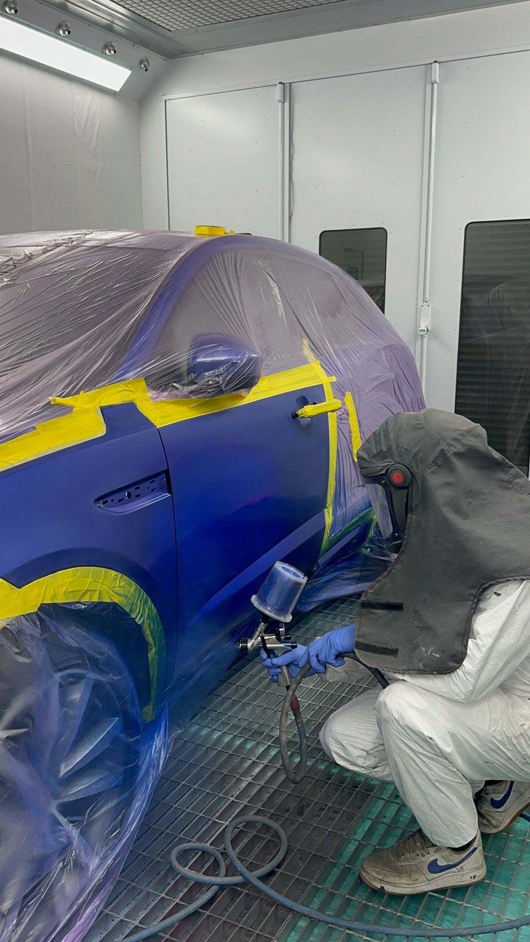 Technician spraying a blue car in the paint booth
